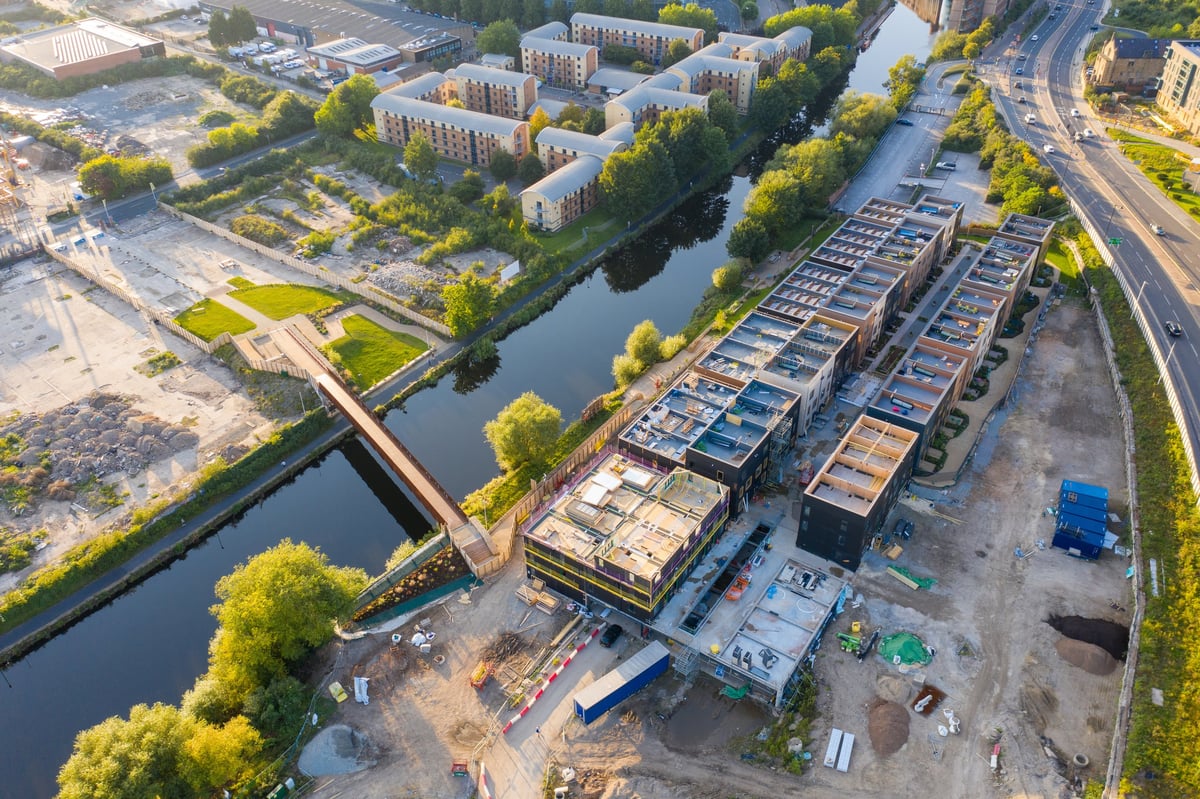 Aerial view of industrial waterfront with barges docked along canal, residential buildings, green spaces, and bridge crossing water