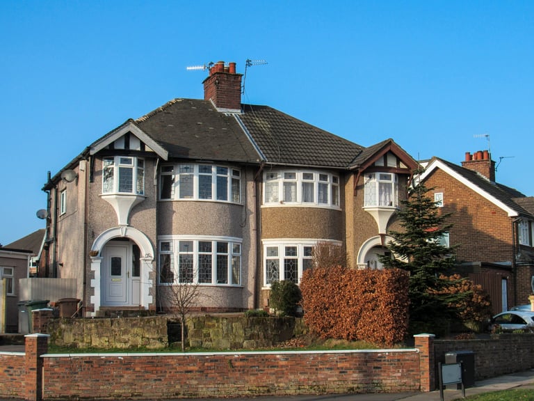 Semi-detached brick house with bay windows, dark roof, and ivy-covered wall against clear blue sky
