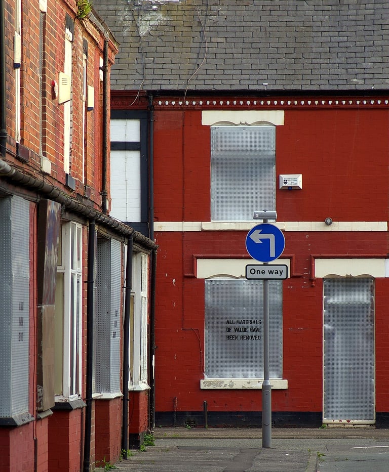 Street view of red brick building with blue one-way arrow sign and metal-shuttered storefront