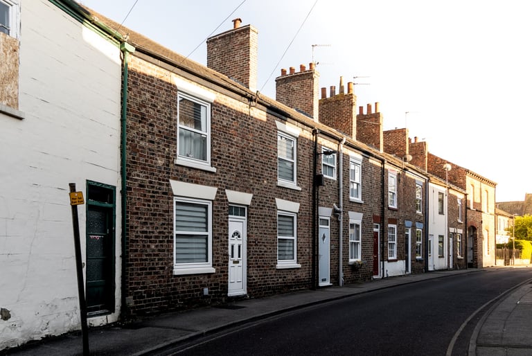 Row of traditional brick and white-painted terraced houses with chimneys lining a quiet street