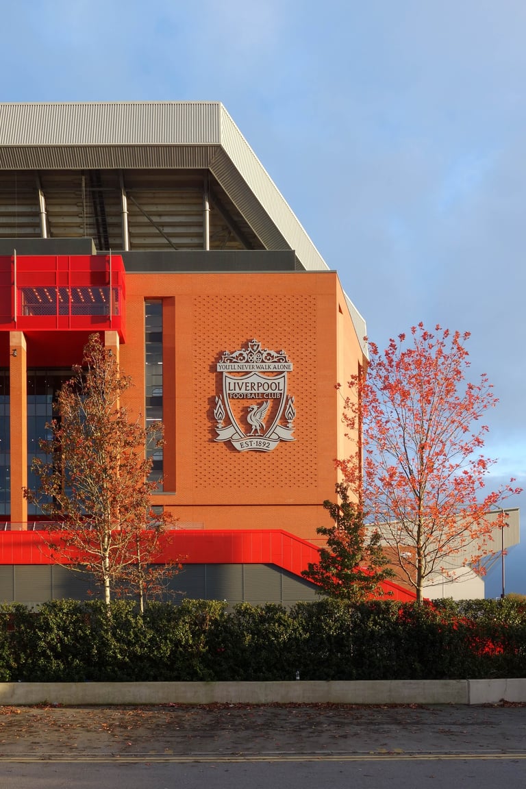Liverpool FC stadium exterior with distinctive red-brick architecture, club crest, and autumn foliage